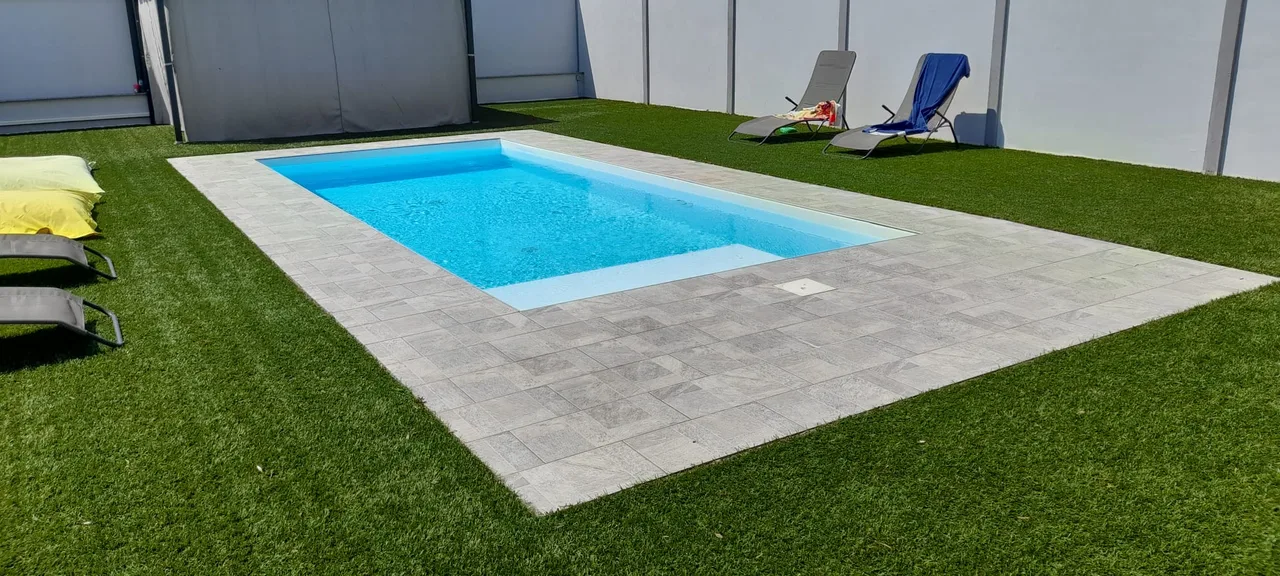 Piscina rettangolare con bordo chiaro e prato